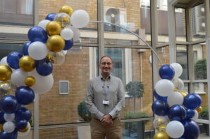 Patrick Maxwell smiling under a balloon arch at the addictions alumni event