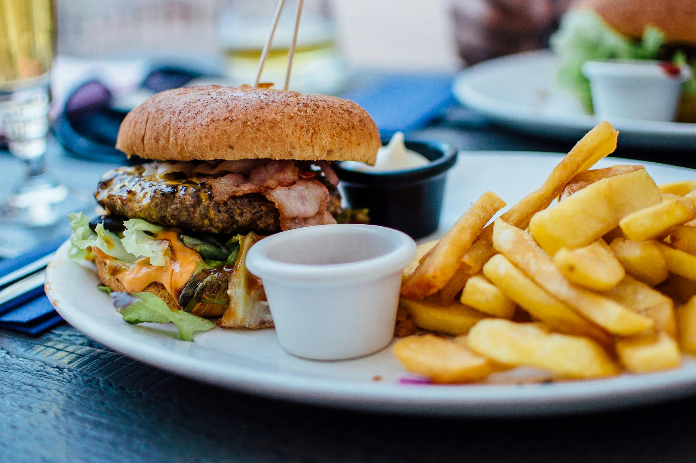 A picture of a burger, fries and sauce on a plate in a restaurant